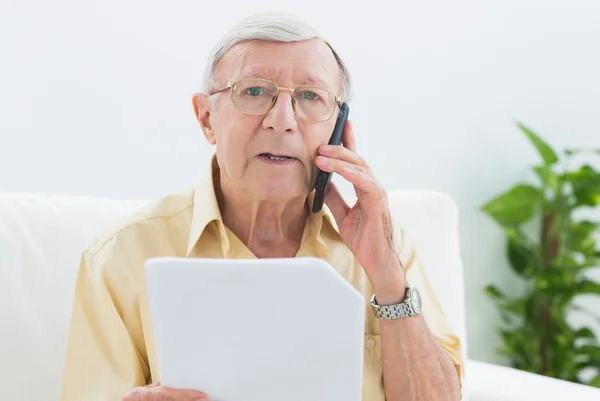 Elderly stern man reading papers on the phone — Stock Photo, Image