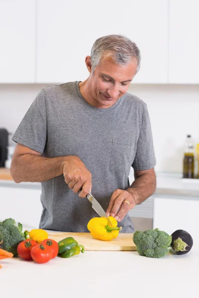 Homem alegre cortando uma pimenta amarela — Fotografia de Stock