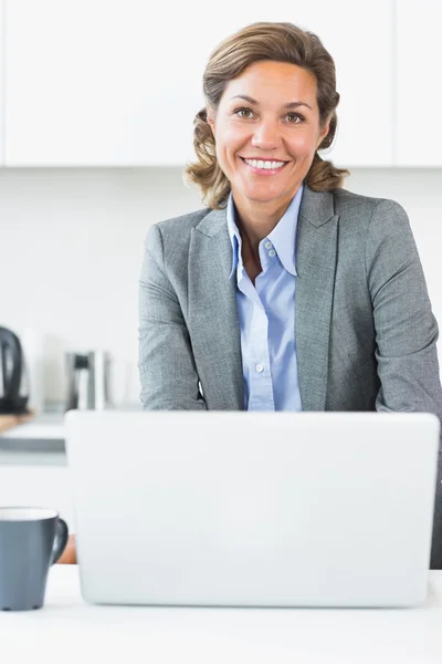 Ευτυχισμένη γυναίκα χρησιμοποιώντας φορητό υπολογιστή στην κουζίνα — Φωτογραφία Αρχείου