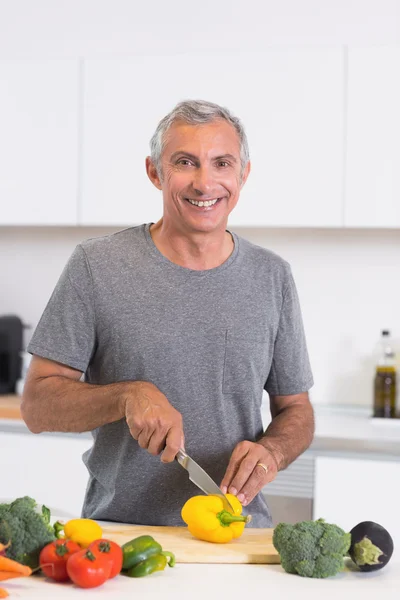 Uomo sorridente che taglia un pepe giallo — Foto Stock