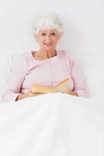 Улыбающаяся женщина читает в постели — стоковое фото