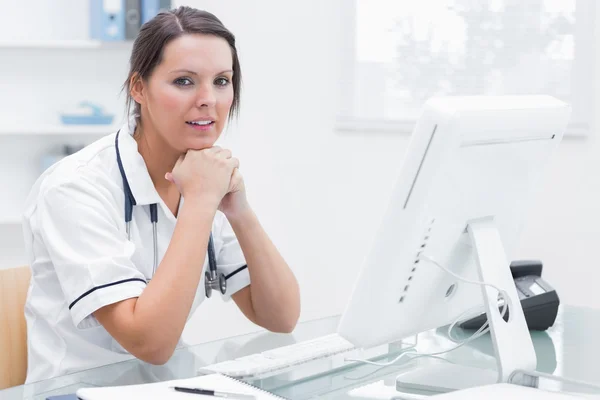 Met handen onder kin achter computer bij kliniek verplegen — Stockfoto