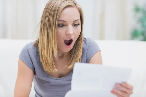 Chockad kvinna läser brev i vardagsrum — Stockfoto