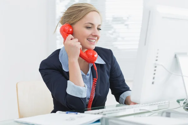 Vrouwelijke uitvoerend met behulp van rode grond lijn telefoon op Bureau — Stockfoto