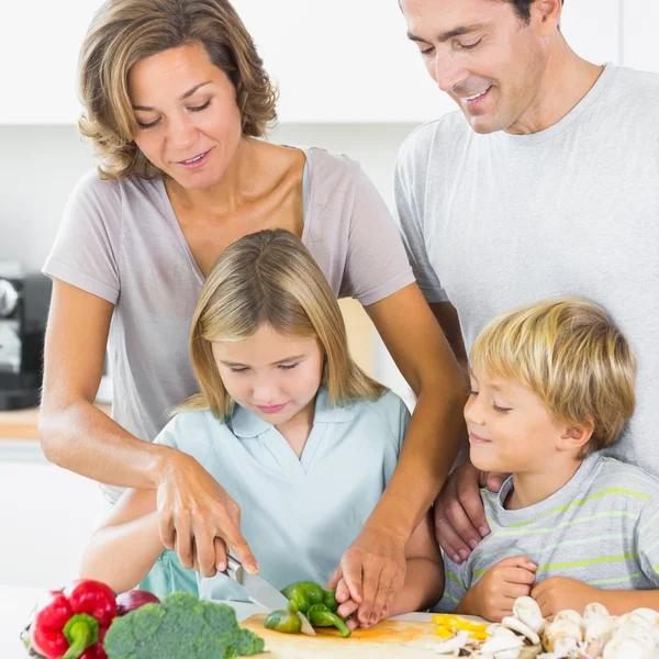 Mother teaching daughter to slice vegetables as father and son a — Stock Photo, Image