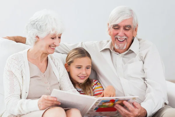 Happy little girl reading with grandparents — Stock Photo, Image