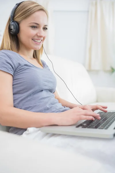 Frau hört Musik über Kopfhörer, während sie Laptop benutzt — Stockfoto