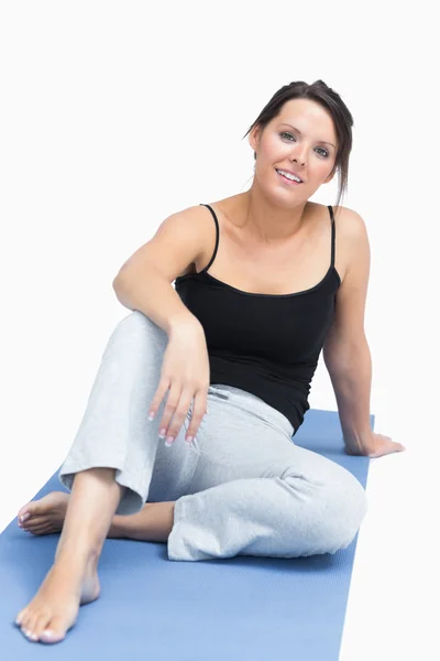 Portret van een jonge vrouw in sportkleding zittend op yoga mat — Stockfoto