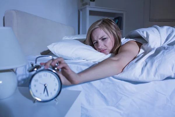 Mujer en la cama extendiendo la mano al despertador — Foto de Stock