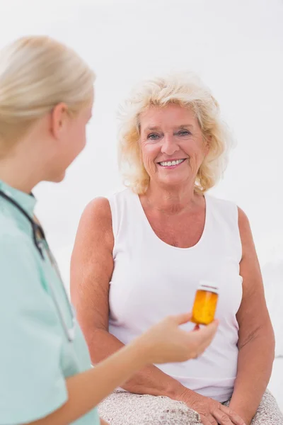 Verpleegkundige over een pil fles aan haar lachende patiënt — Stockfoto