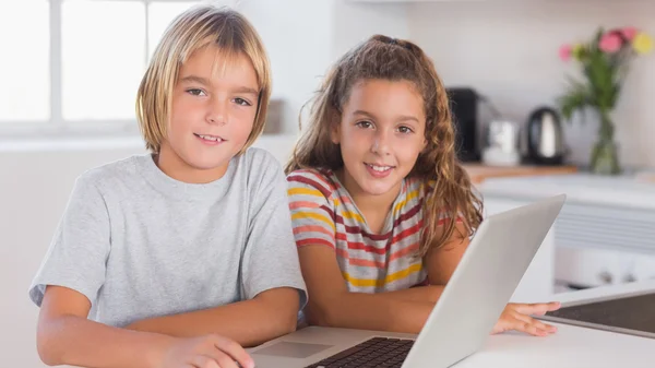 Due bambini che guardano la fotocamera insieme al computer portatile di fronte — Foto Stock