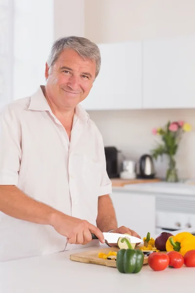 Alter Mann lächelt und schneidet Gemüse — Stockfoto