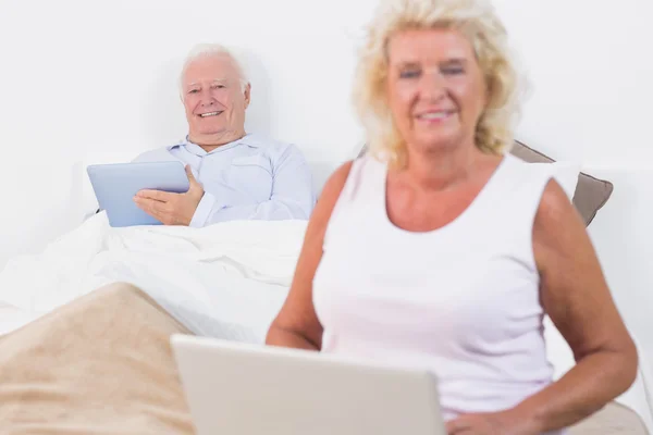 Улыбающаяся пожилая пара с помощью планшета и ноутбука — стоковое фото
