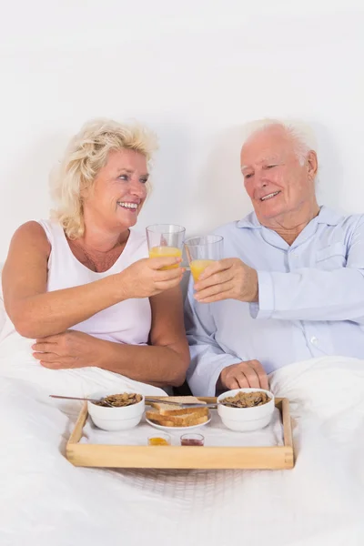 Altes Paar stößt beim Frühstück mit Orangensaft an — Stockfoto