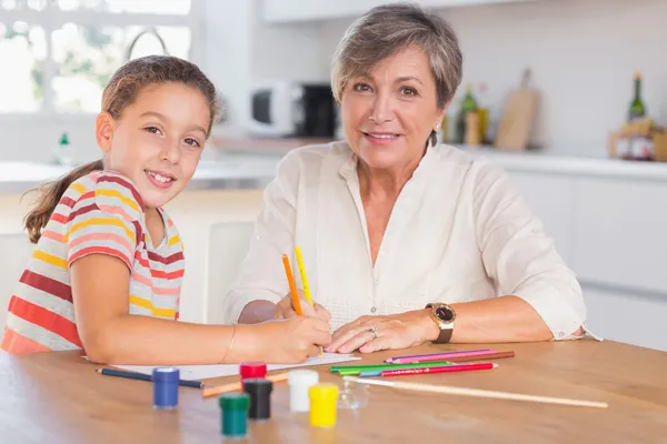 Niña con su abuela mirando a la cámara mientras dibuja — Foto de Stock