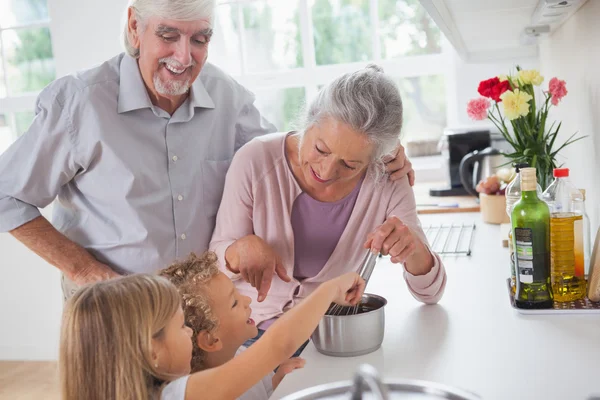 Abuelos sonrientes ayudando a los niños a cocinar —  Fotos de Stock