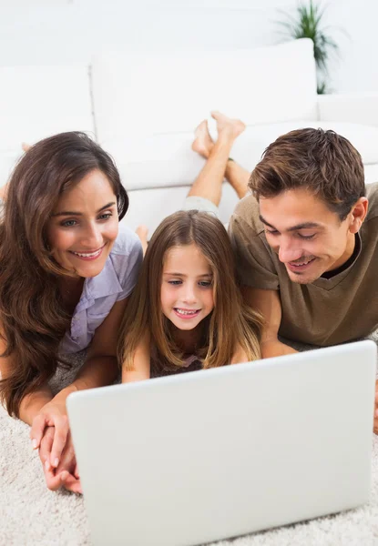 Familia acostada en una alfombra con el portátil — Foto de Stock