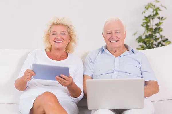 Lachende oude paar met behulp van een laptop en de tablet — Stockfoto