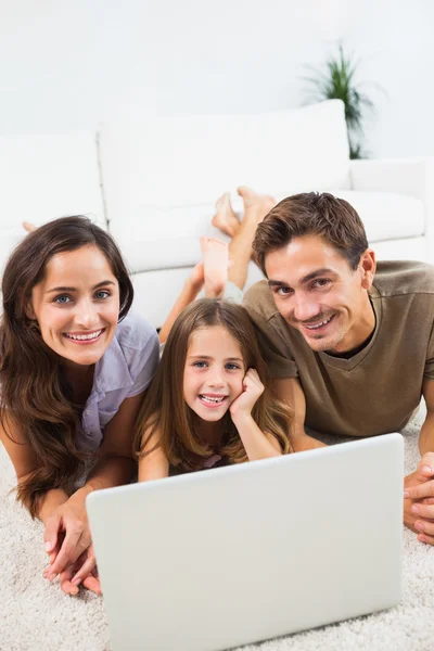 Familia sonriente acostada en una alfombra con el portátil — Foto de Stock