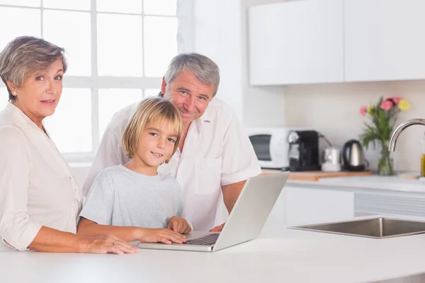 Kind und Großeltern blicken mit Laptop in die Kamera — Stockfoto