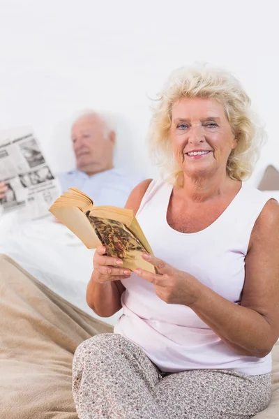 Smiling aged couple reading book and newspaper — Stock Photo, Image