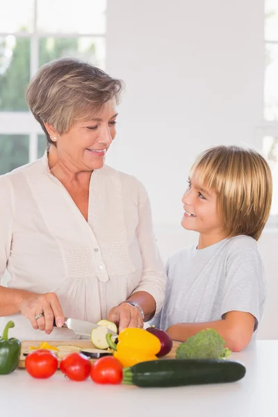 Grootmoeder snijden groenten kijken naar kleinzoon — Stockfoto