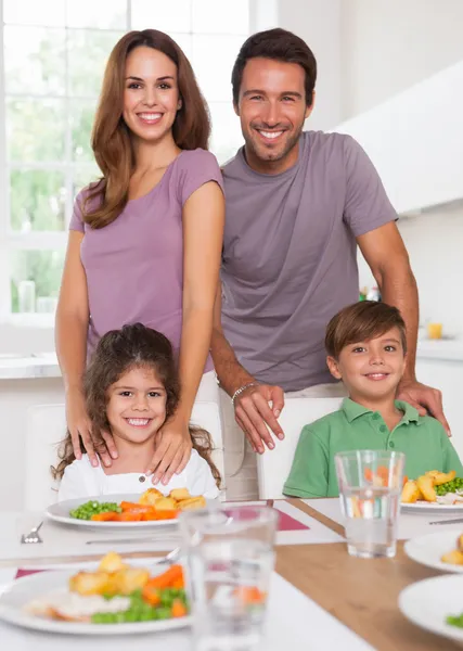 Zwei Kinder und ihre Eltern lächeln beim Abendessen in die Kamera — Stockfoto