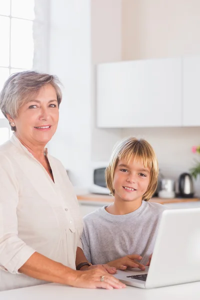Niño y abuela mirando cámara con un ordenador portátil — Foto de Stock