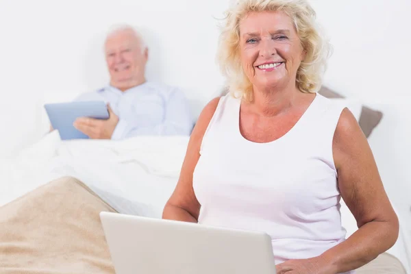 Coppie anziane sorridenti usando una targa e il computer portatile — Foto Stock