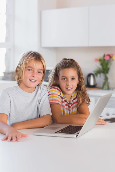 Duas crianças olhando para a câmera com laptop na frente — Fotografia de Stock