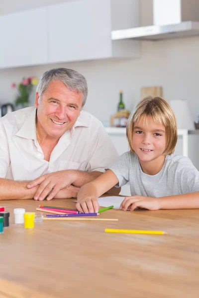 Barnbarn och farfar tittar på kameran med ritningar — Stockfoto