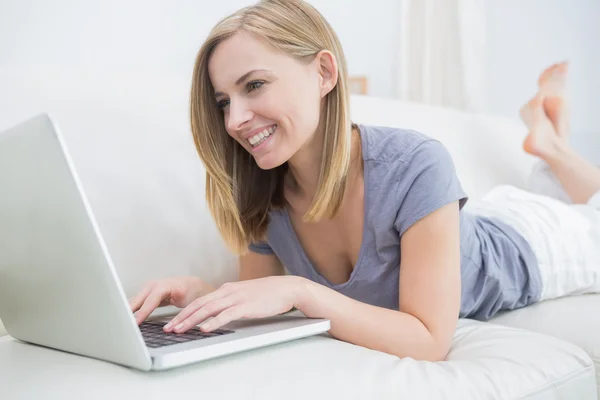 Casual woman lying on couch and using laptop Royalty Free Stock Photos