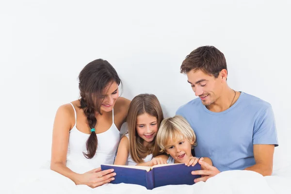 Family sitting with a storybook on the bed — Stock Photo, Image