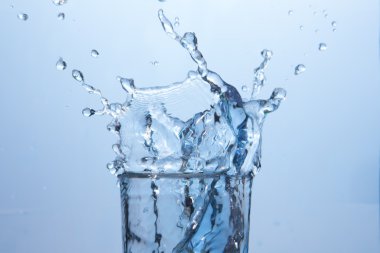 Close up on ice cube falling into glass of water clipart