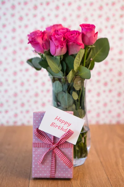 Bando de rosas cor-de-rosa em vaso com presente rosa encostado a ele um — Fotografia de Stock