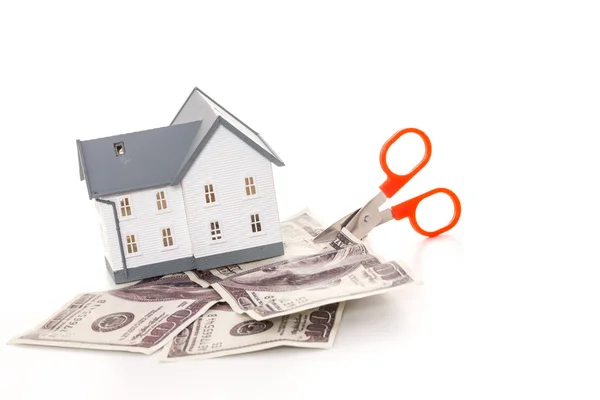 Scissors cutting through dollar bills under model house — Stock Photo, Image