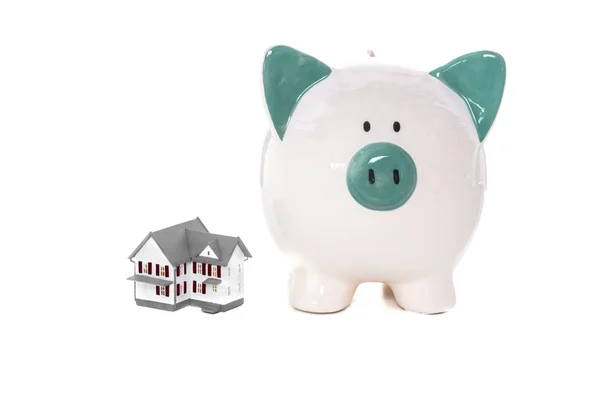 Green and white piggy bank standing beside miniature home — Stock Photo, Image