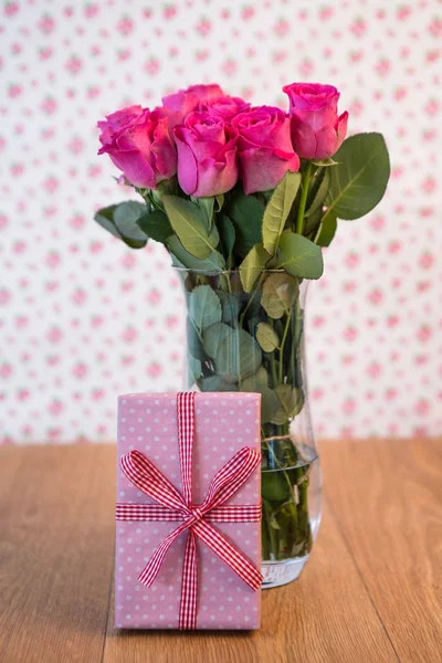 Bando de rosas cor-de-rosa em vaso com presente rosa encostado a ele — Fotografia de Stock