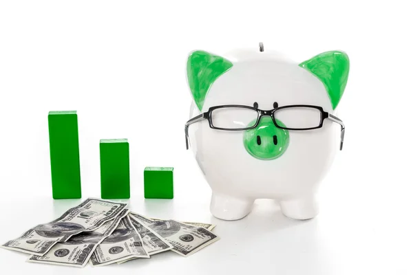 Piggy bank wearing glasses with dollars and green graph model — Stock Photo, Image