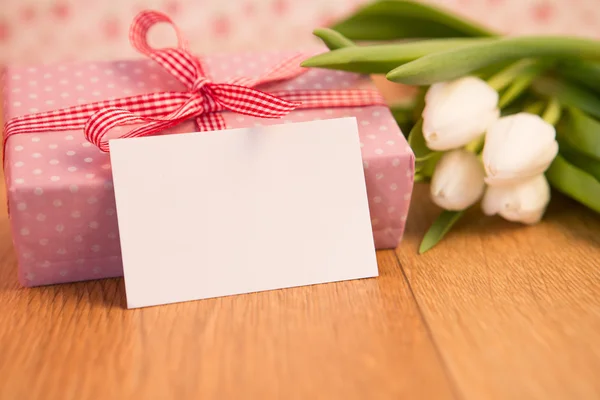 Pink wrapped present with bunch of white tulips and blank card — Stock Photo, Image