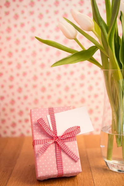 Vaas met tulpen op houten tafel met roze gewikkeld geschenk en blanco — Stockfoto