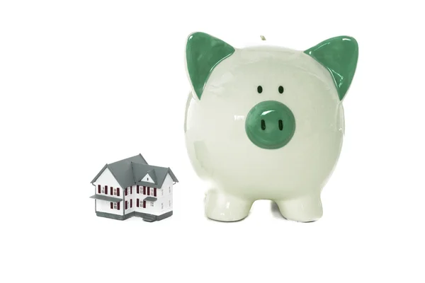 Groene piggy bank staande naast miniatuur thuis — Stockfoto