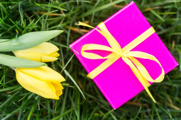 Różowe pudełko z żółtą Wstążkę i żółte tulipany — Zdjęcie stockowe