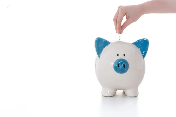 Hand placing coin into blue and white piggy bank — Stock Photo, Image