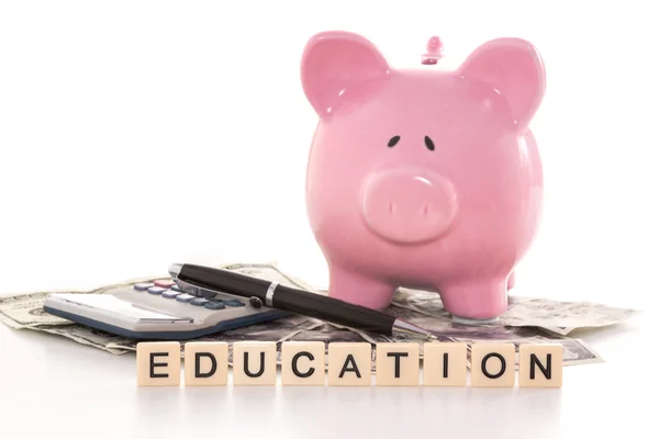 Piggy bank beside calculator and education spelled out in plasti — Stock Photo, Image