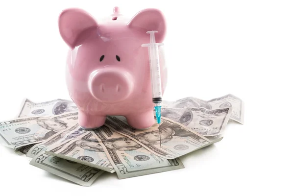 Sparschwein und Spritze auf einem Haufen Dollars — Stockfoto