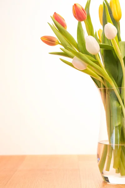 Skleněná váza tulipány na dřevěný stůl — Stock fotografie