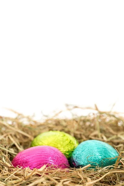 Drie folie verpakt paaseieren genesteld in stro nest — Stockfoto