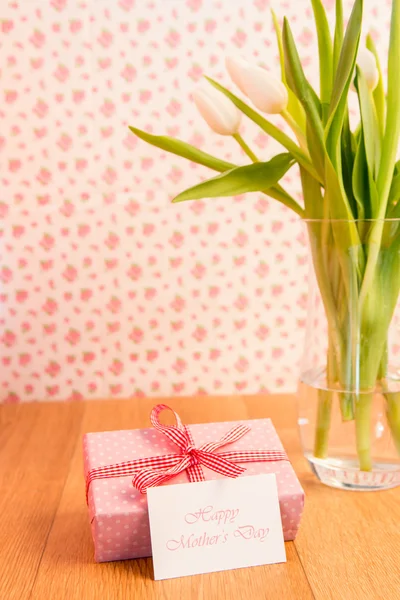 Pink wrapped present with mothers day card beside vase of tulips Stock Photo