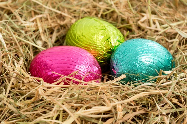 Tres coloridos huevos de Pascua enclavados en un nido de paja — Foto de Stock